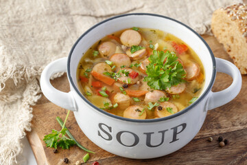 Fresh hot soup with meat sausage slices, beans, carrot, pasta and green herbs in bowl on wooden...