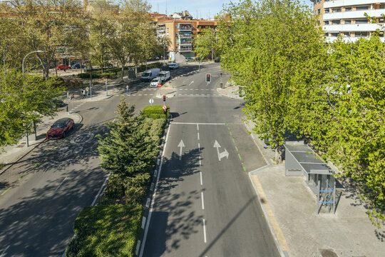 A city street with a median lined with trees, hedges and plants and furniture from a gray bus stop on one side
