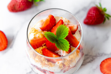 Strawberry trifle dessert with custard, cake crumb and fresh strawberry in glass on marble. Recipe of simple layered dessert with fresh berry and jam. Top view strawberry dessert.