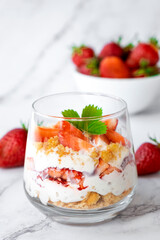 Strawberry dessert in glasses with whipped cream, cookie and fresh strawberry in glass on marble background. Recipe of simple healthy homemade organic dessert, cheesecake, mousse or berry trifle cake.