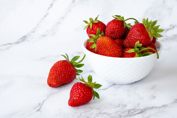 Heap of juicy strawberries in ceramic bowl on marble background. Healthy eating, fruit diet and detox food concept. Close up fresh farm berry.