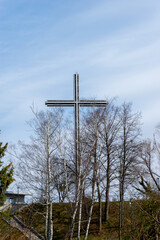 Cross on top of a hill with bare trees against a blue sky