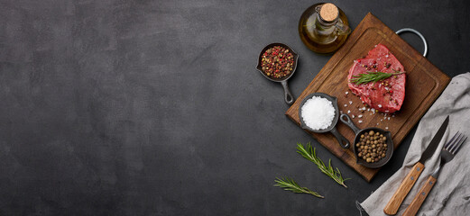 Obraz na płótnie Canvas Raw piece of beef with spices pepper, rosemary sprig, salt and olive oil on a wooden board, black background