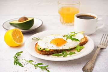 Delicious sandwich with fried egg, arugula and avocado on light background