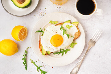 Delicious sandwich with fried egg, arugula and avocado on light background