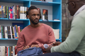 Portrait of black young man talking to therapist of guidance counsellor in college library