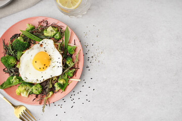 Plate with tasty fried egg and salad on grey background