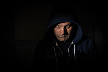 Unshaved face of mid aged male wearing a hood in a dark room