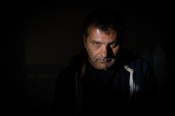 Fototapeta premium A striking portrait captured on a black backdrop with distinct shadows, featuring a male model in his fifties from the Balkan region who is staring directly at the camera with an unshaven face.