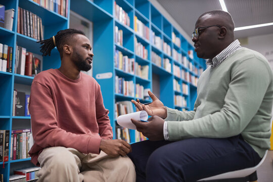 Side view portrait of African American male therapist talking to student in mental health session and holding clipboard