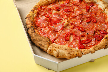 Cardboard box with delicious pepperoni pizza on yellow background