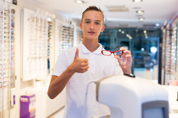 Male client standing with new spectacles and thumb up in medical shop