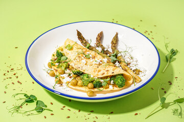 Tasty omelet with broccoli, pea and asparagus on green background