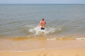 A man runs into the water. Sea spray from splashing. The sea coast.