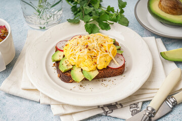 Plate with tasty scrambled eggs sandwich and vegetables on light background