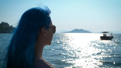 Female with blue hair by the sea. A young girl looks at the sunny path to the sea.