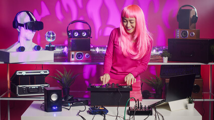Artist with pink hair dancing and having fun mixing sound during night time in club, performing eletronic music using professional mixer console. Performer recording album using audio equipment