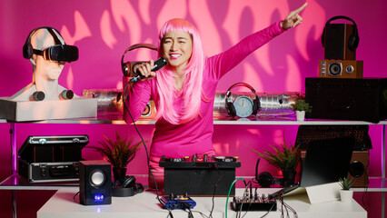 Cheerful performer having fun mixing techno sounds in night club, playing music using professional turntables. Asian artist standing at dj table dancing while celebrating techno album with fans