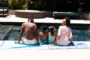 Rear view of african american parents and children sitting at poolside at resort on sunny day