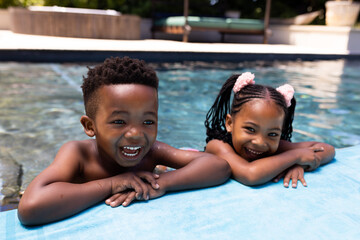 Portrait of cheerful african american siblings laughing while relaxing at poolside in resort