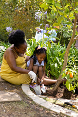 African american grandmother and granddaughter digging soil with tools while gardening in yard