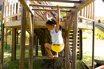 African american girl hanging on wooden monkey bars while playing in playground