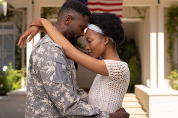 Side view of african american army soldier husband and wife with head to head standing outside house