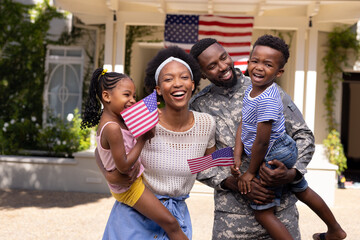 African american soldier husband and mother carrying children with flags of america outside house