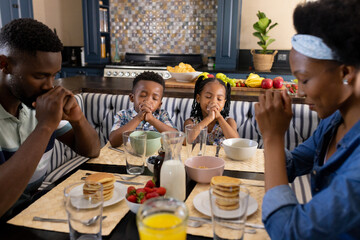 African american parents and children saying grace at dining table before breakfast in morning