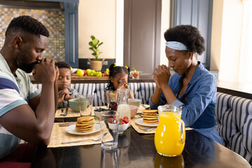 African american parents with children praying before breakfast at dining table in morning