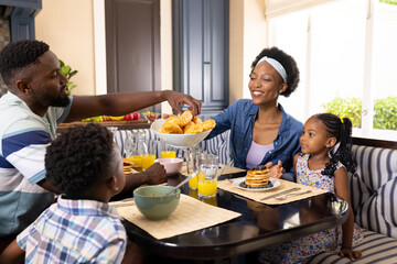 African american woman sharing croissant with husband while having breakfast with children at table