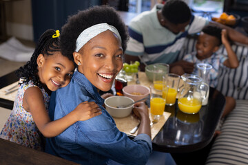 High angle portrait of cheerful african american mother and daughter sitting at dining table at home