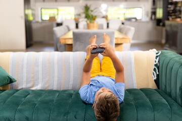 Obraz premium Caucasian boy using mobile phone while lying on sofa in living room, copy space