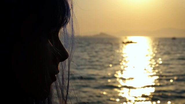 Teen silhouette by dark beach. A sad teen girl enjoy the evening sea from the shore in summer.