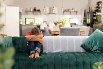Full length of caucasian boy hugging knees while sitting on sofa in living room, copy space