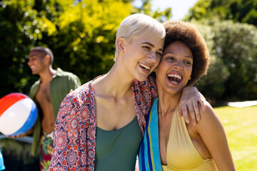 Happy diverse female friends having pool party, embracing and smiling in garden