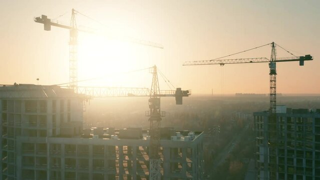 Aerial side view of a tower cranes silhouettes at the construction site of a residential building 