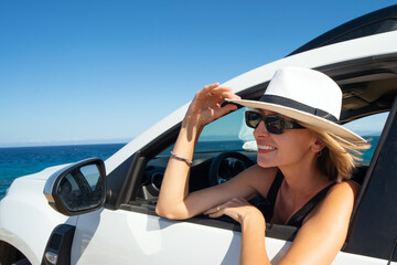 Happy woman holding summer hat outside open window in car. People lifestyle. Traveler on road trip.