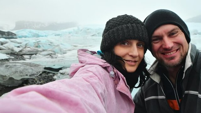 Happy multiethnic couple taking selfie in front of glacier lagoon in Iceland. Two tourists having fun on romantic winter vacation in Iceland - Holidays and traveling lifestyle