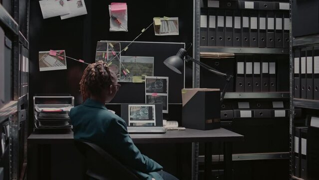 African american police investigator reading case file in incident room. Woman detective holding folder and analyzing investigation report, looking at criminal records to find suspect.