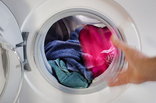 Person Hand wirft W&auml;sche W&auml;schest&uuml;ck in Waschmaschine zum Waschen bef&uuml;llen Waschgang