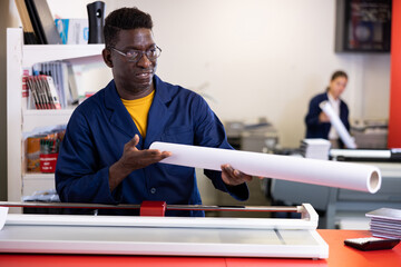 Middle-aged African American male specialist in uniform holding whatman in a roll in the middle of print shop