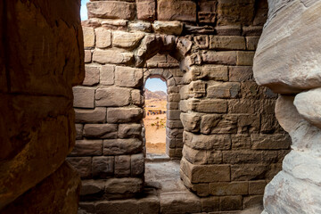 View through an arched stone brick window from the hillside site of the ancient Urn Tomb in the Habatean Rose City of Petra Jordan, in the Wadi Musa desert. - obrazy, fototapety, plakaty