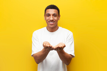 young African American guy holds his hands in front of him on yellow isolated background, man holds nothing - obrazy, fototapety, plakaty