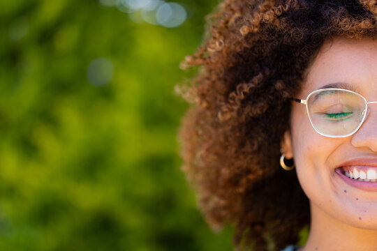 Cropped face of biracial young woman with eyes closed and afro hair smiling in yard