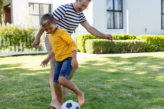 Cheerful caucasian grandfather and grandson playing soccer on grassy field in yard, copy space