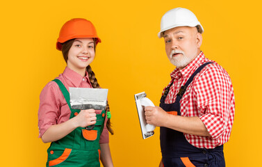 happy child and grandfather plasterer in hard hat on yellow background