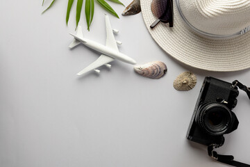 Airplane model, straw hat, sunglasses, camera and seashells on white background with copy space