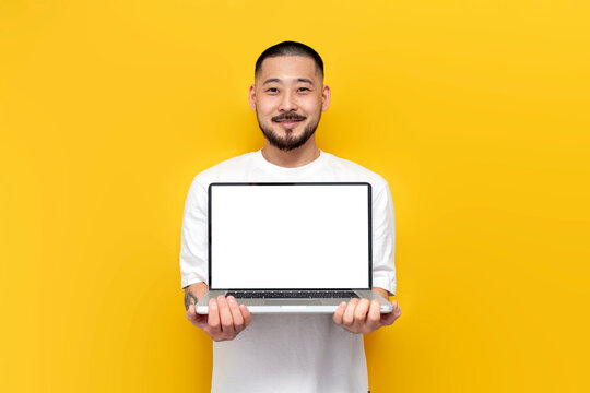 asian man in white t-shirt shows blank laptop screen on yellow isolated background