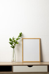 Vertical of empty wooden frame with copy space and plant on table against white wall